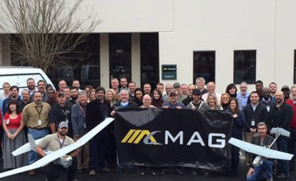 Large group of employees posing behind the MAG sign