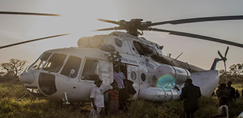 Group of people standing around a helicopter that is sitting in a field