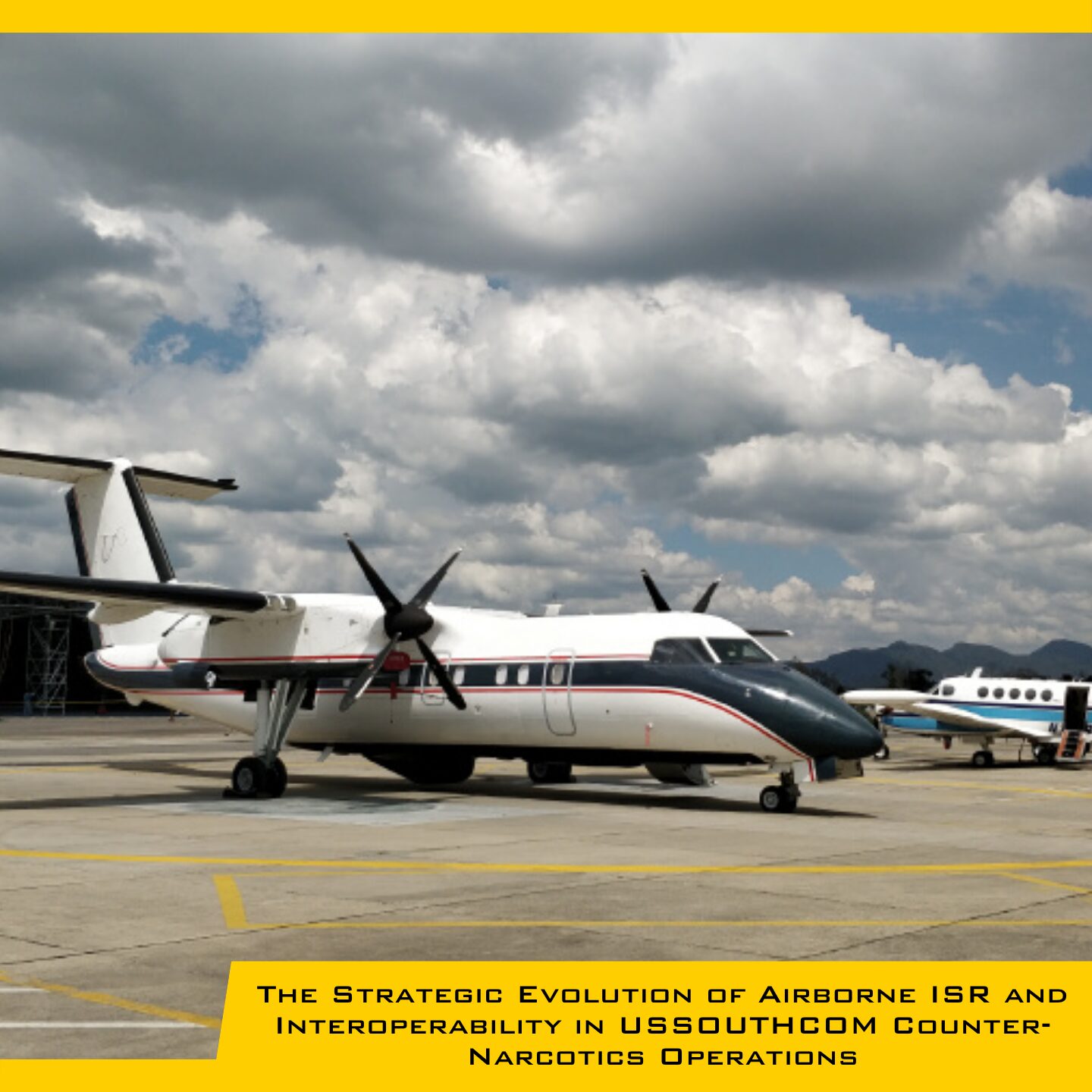 White twin‑prop airplane parked on a runway with a cloudy sky and another aircraft visible in the background.